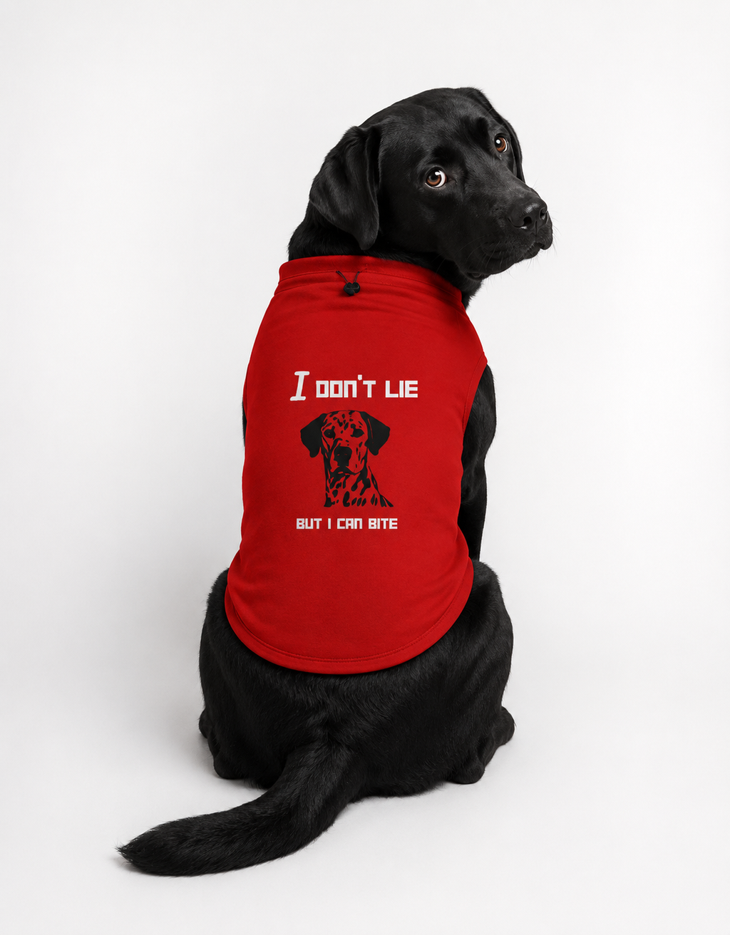 A black Labrador wearing a red sleeveless pet shirt with white text reading 'I don't lie' and a black dog graphic, sitting against a light gray studio background.